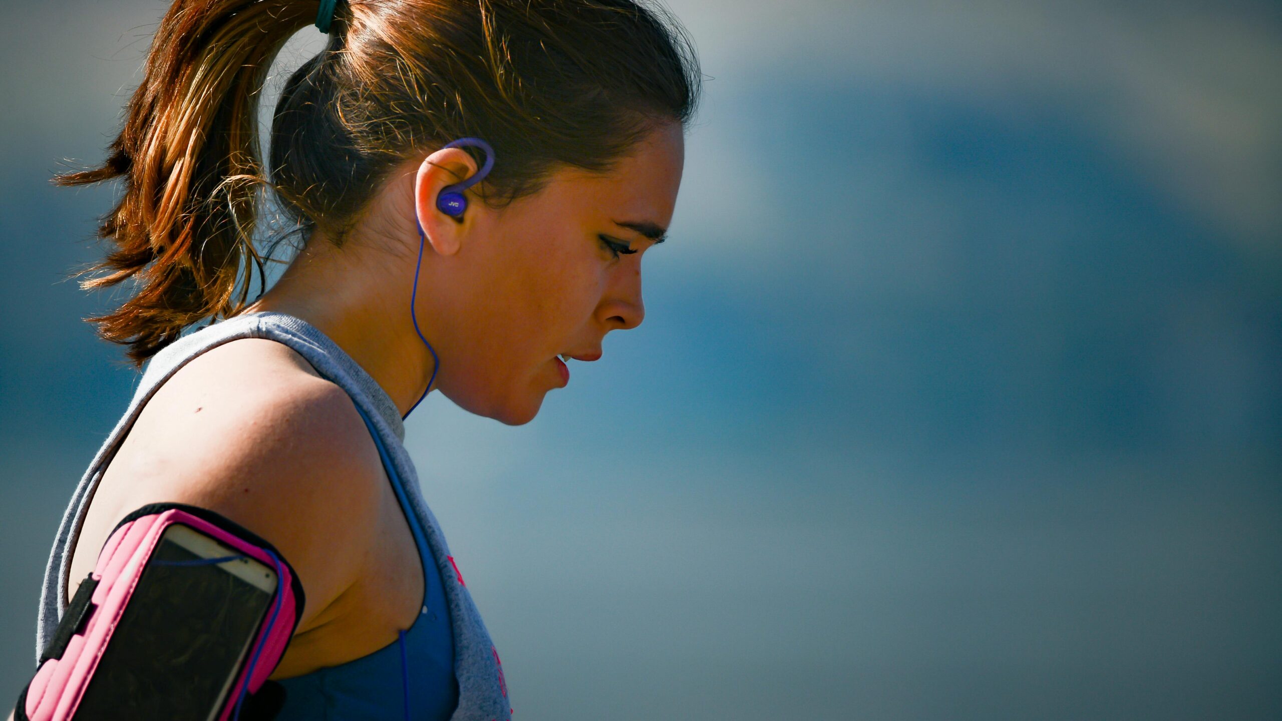 A determined female athlete running in Chelan, WA with earphones, captured in a side profile.